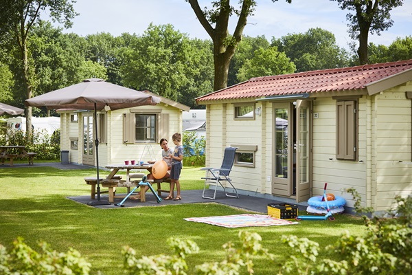 Gezin geniet van een zomerse dag op vakantiepark de Leistert in Leudal, met houten chalets en een picknicktafel in het gras.