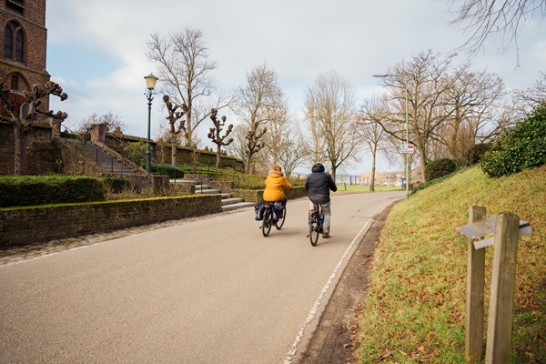 Two cyclists cycle past the Rose Church in Asselt in autumn