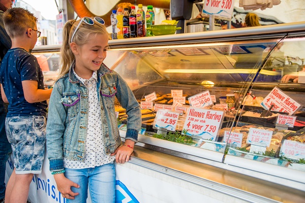A smiling girl at a fish stall at a market in Weert, with herring and other fresh seafood in the display case.