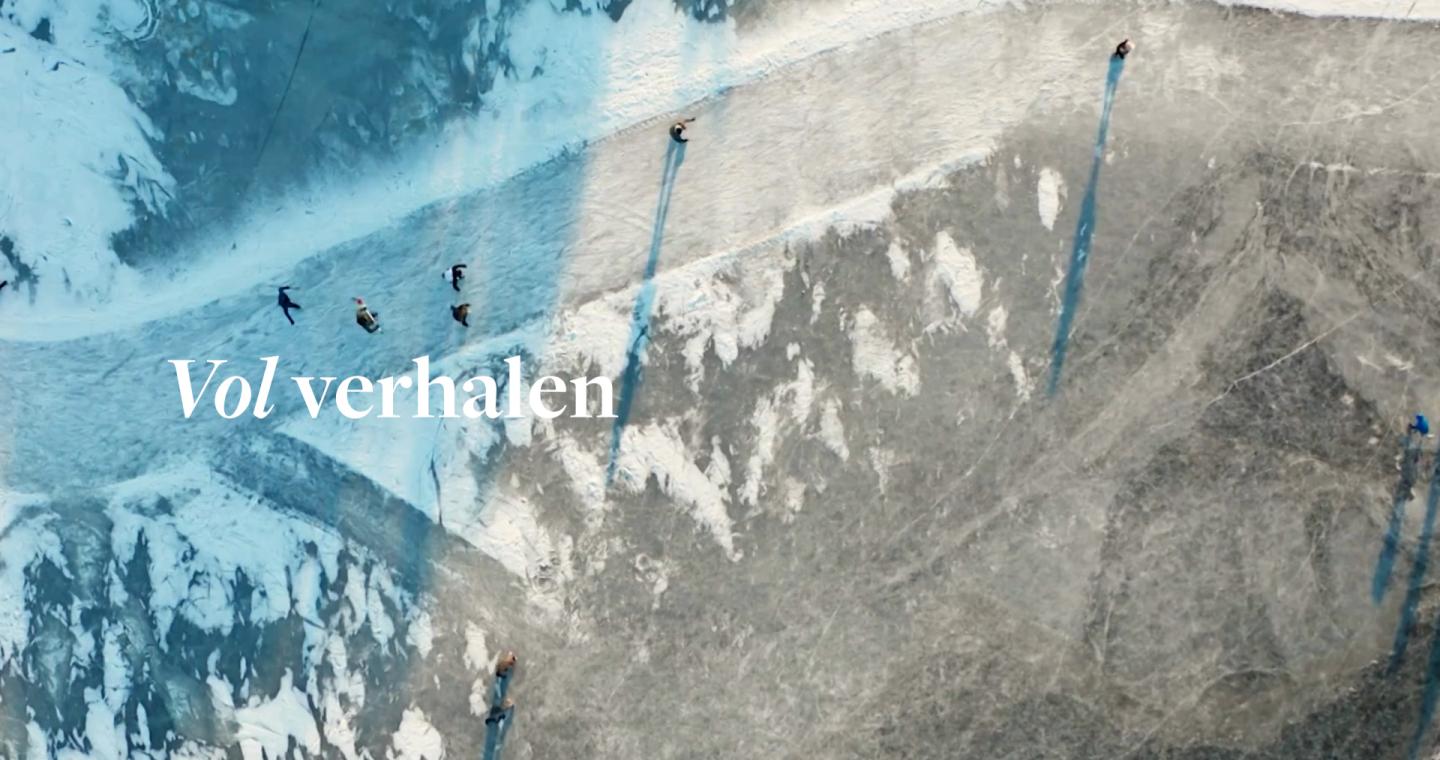 Een bevroren landschap van bovenaf met mensen die schaatsen op het ijs en lange schaduwen werpen in het winterlicht.