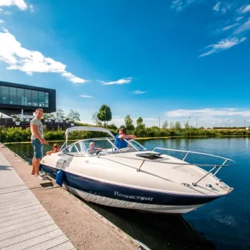 Motorboot met opvarenden aan de steiger bij een moderne jachthaven in Limburg, op een zonnige dag.