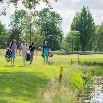 Vier mensen lopen met golftassen over de green bij golfbaan Crossmoor in Weert, op een zonnige dag.