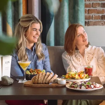 Twee vrouwen genieten van een uitgebreide herfstlunch bij Brasserie LUS in Linne, met verse salades, brood en warme gerechten op tafel in een sfeervolle setting.